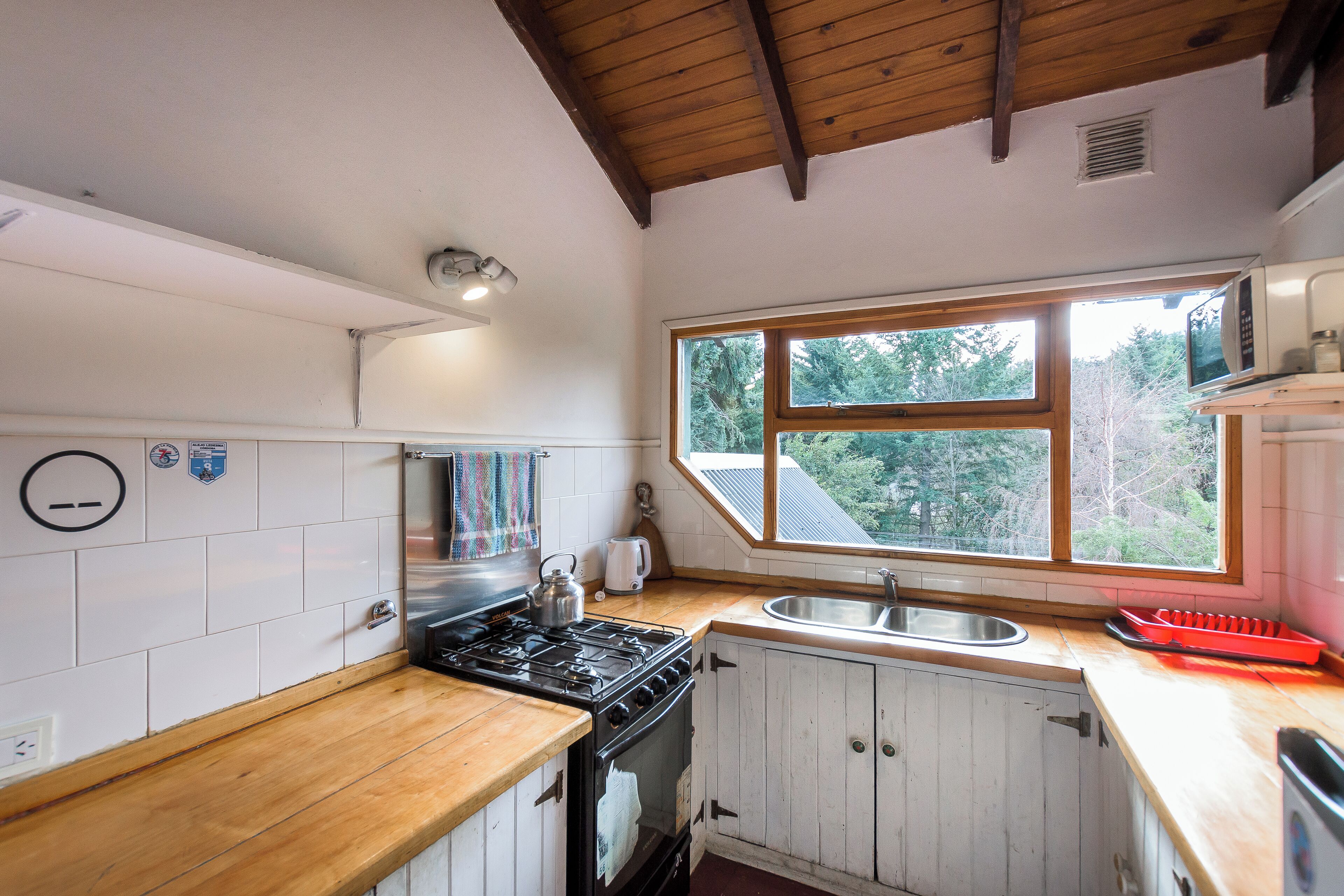 A kitchen with white cabinets, a wooden countertop, a stove, a sink, and a window with a view of trees.
