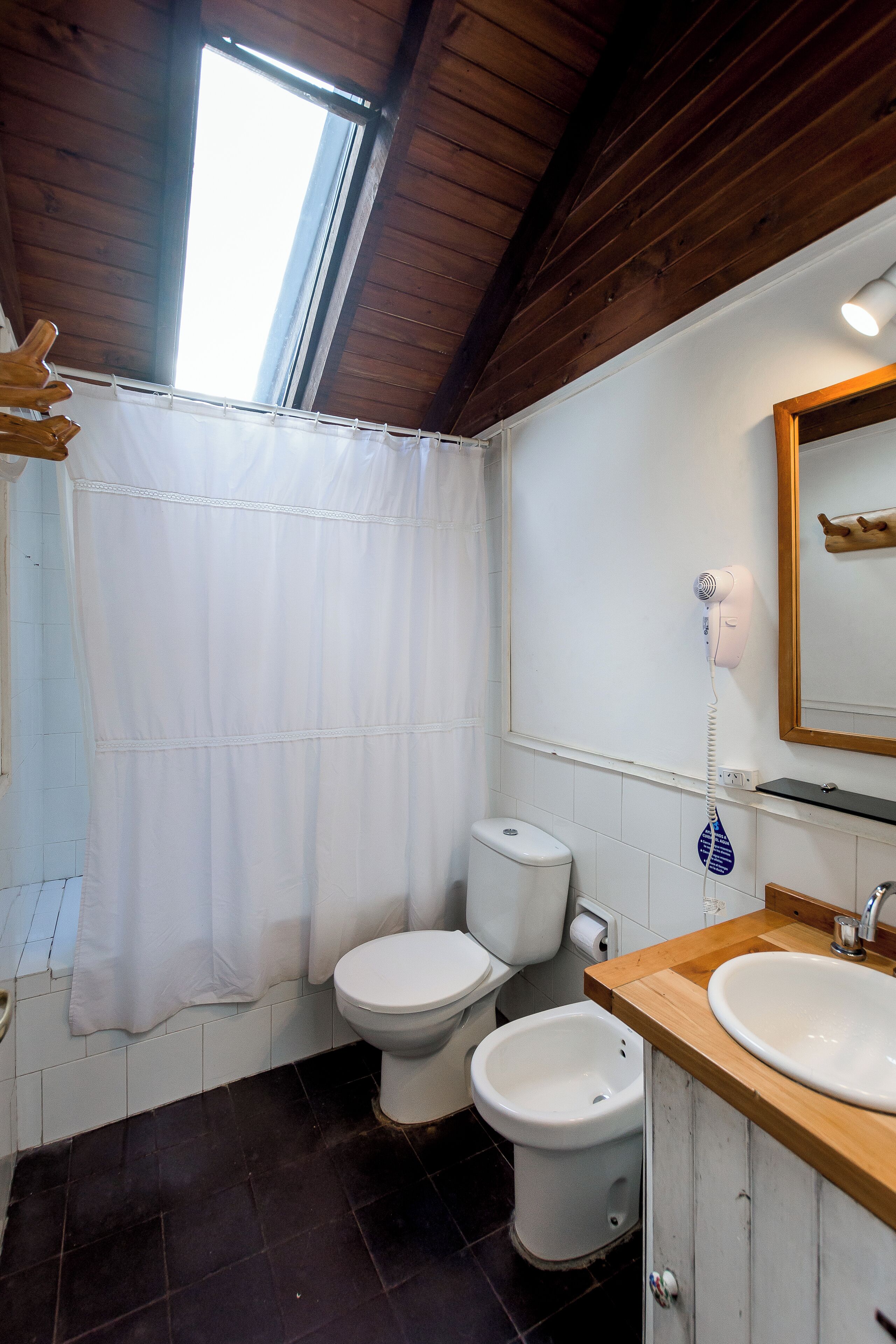 Un baño con cortina de ducha, inodoro, bidé, lavamanos y un secador de pelo montado en la pared.