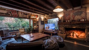A cozy living room with a stone fireplace, wooden furniture, and a television displaying an elk.