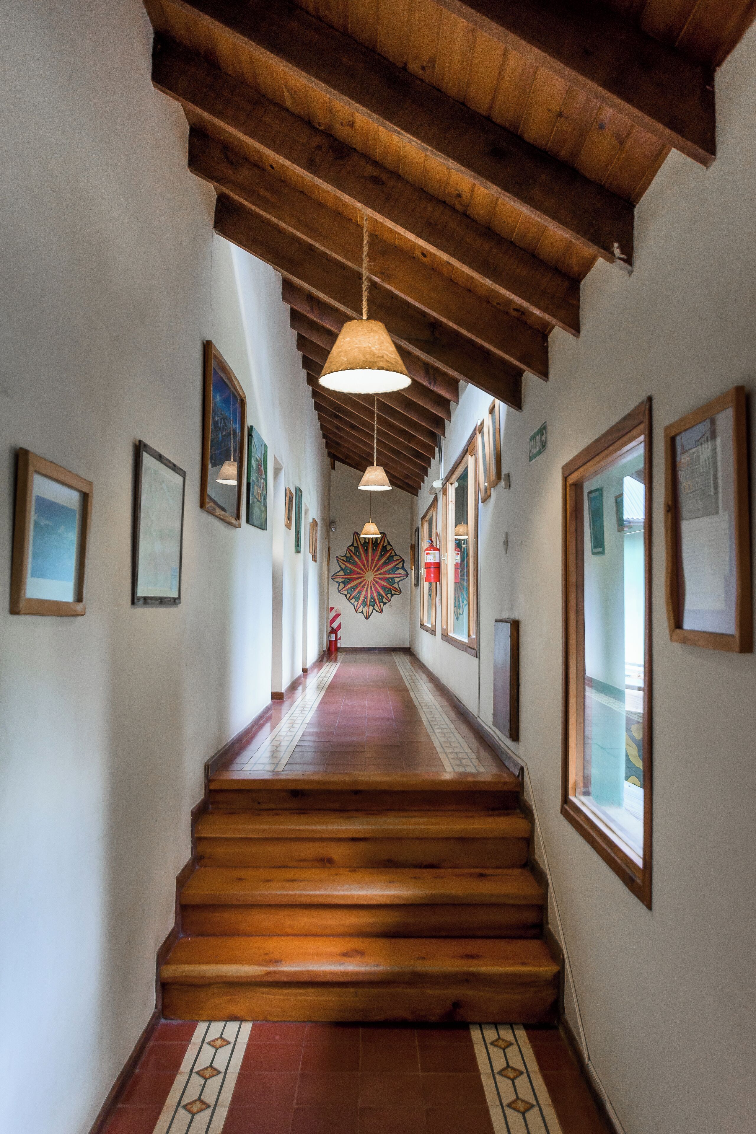 A hallway with wooden stairs, framed artwork on the walls, and a hanging light fixture.