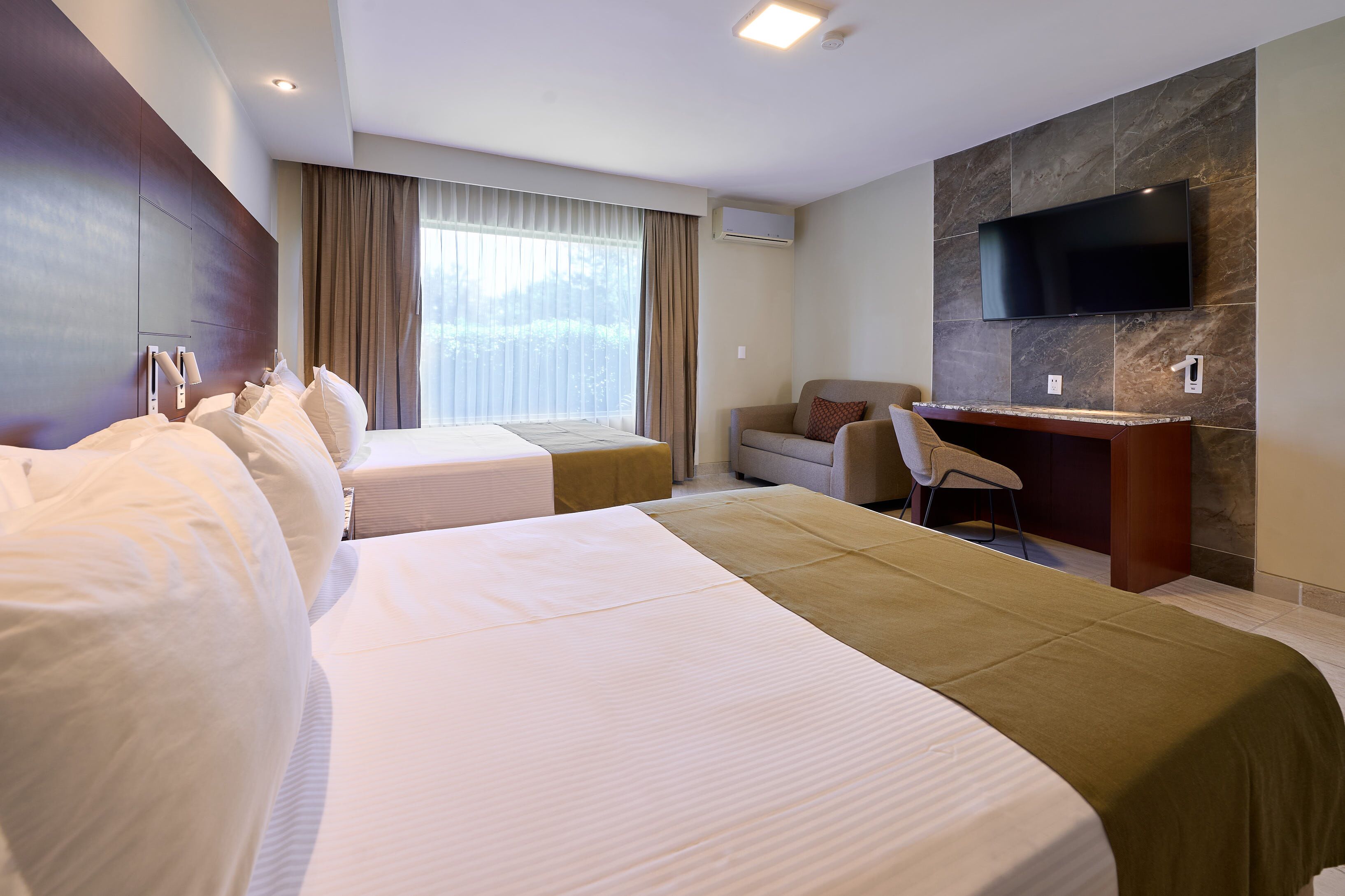 Habitación de hotel con dos camas, un escritorio, una silla, un televisor y una ventana con cortinas.