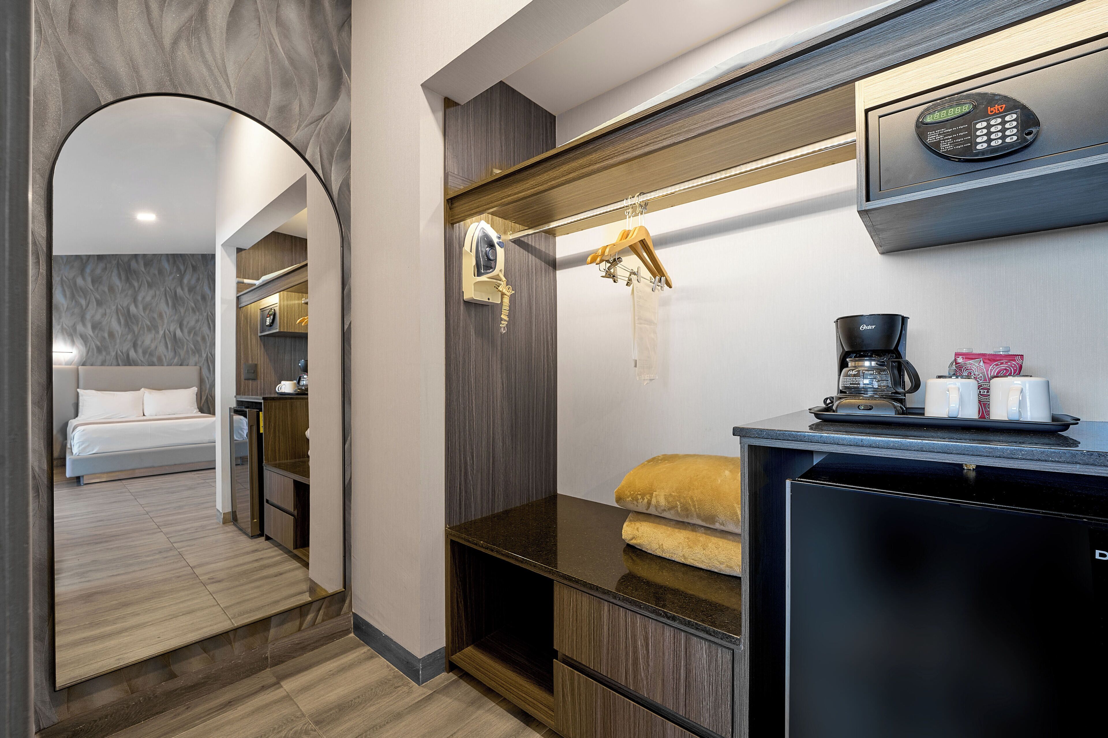 A modern hotel room with a bed, a small kitchenette, a coffee machine, and a hanging coat rack.