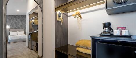 A modern hotel room with a bed, a small kitchenette, a coffee machine, and a hanging coat rack.