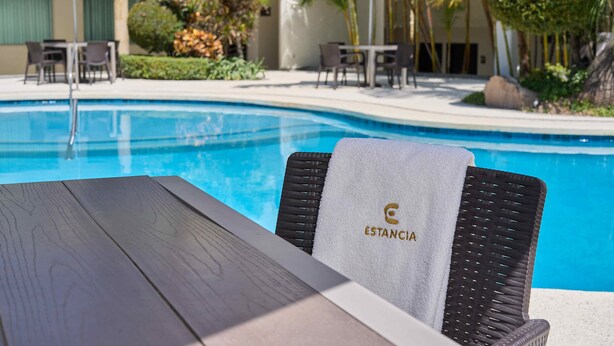 A poolside area with a lounge chair, a table, and a view of the pool. - Hotel Estancia Business Class (Guadalajara)