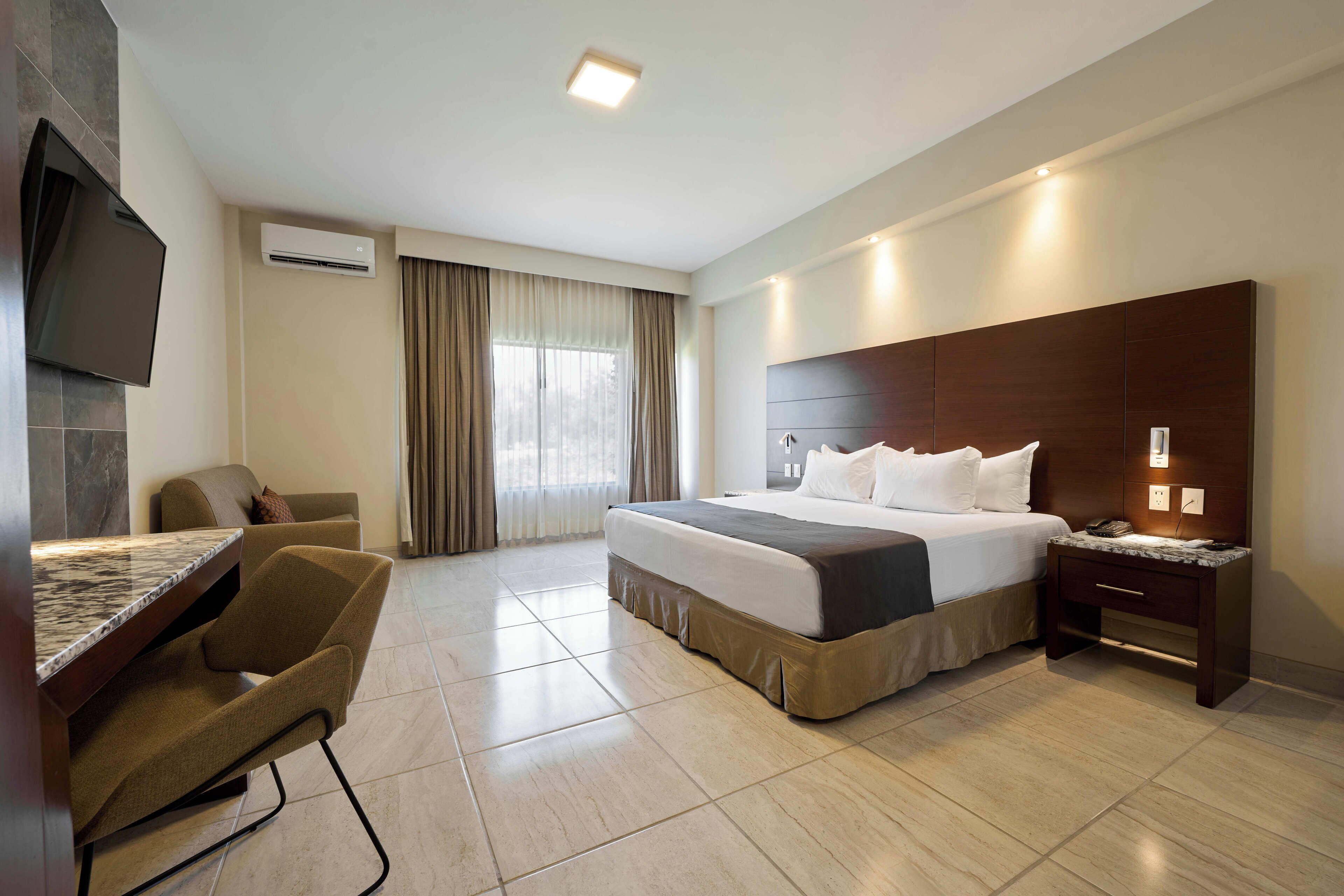 Ein Hotelzimmer mit einem Bett, einem Schreibtisch, einem Sessel, einem Fernseher und einem Nachttisch.