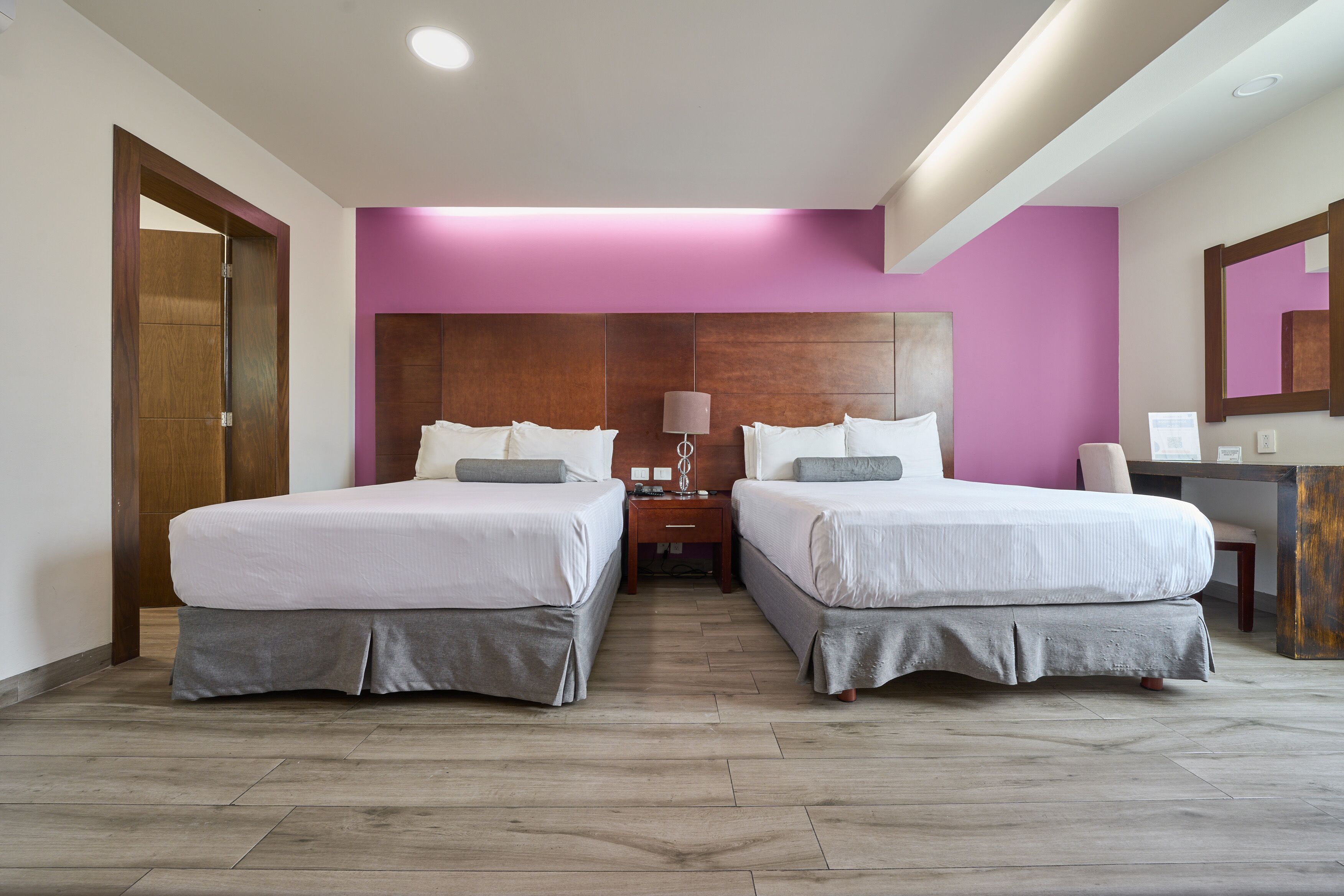 Habitación de hotel con dos camas, cabecera de madera, un escritorio y un espejo.