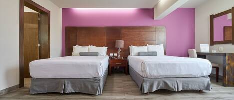 A hotel room with two beds, a wooden headboard, a desk, and a mirror.