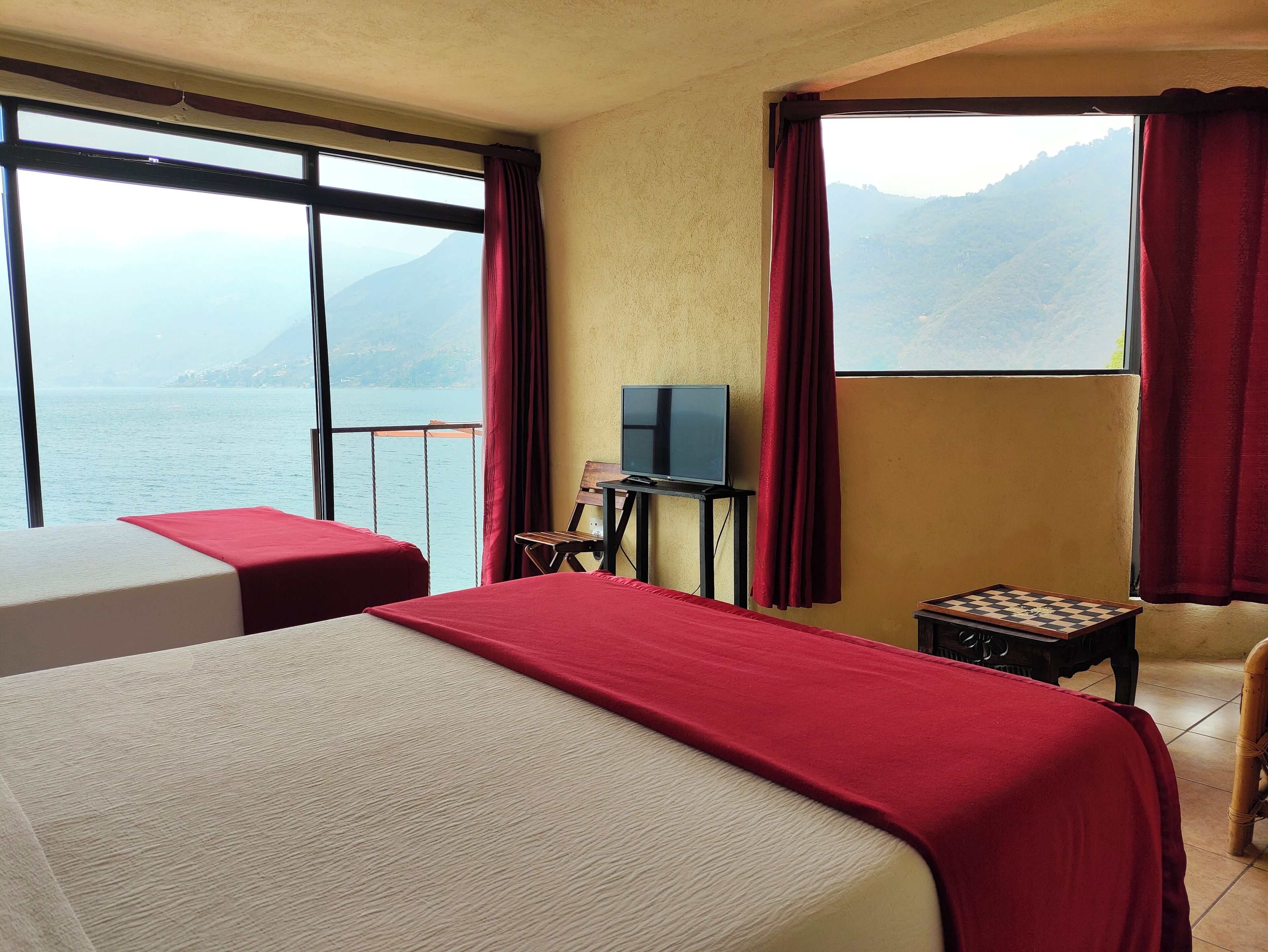 Habitación de hotel con dos camas, televisión, una mesita y vistas al mar y a las montañas.
