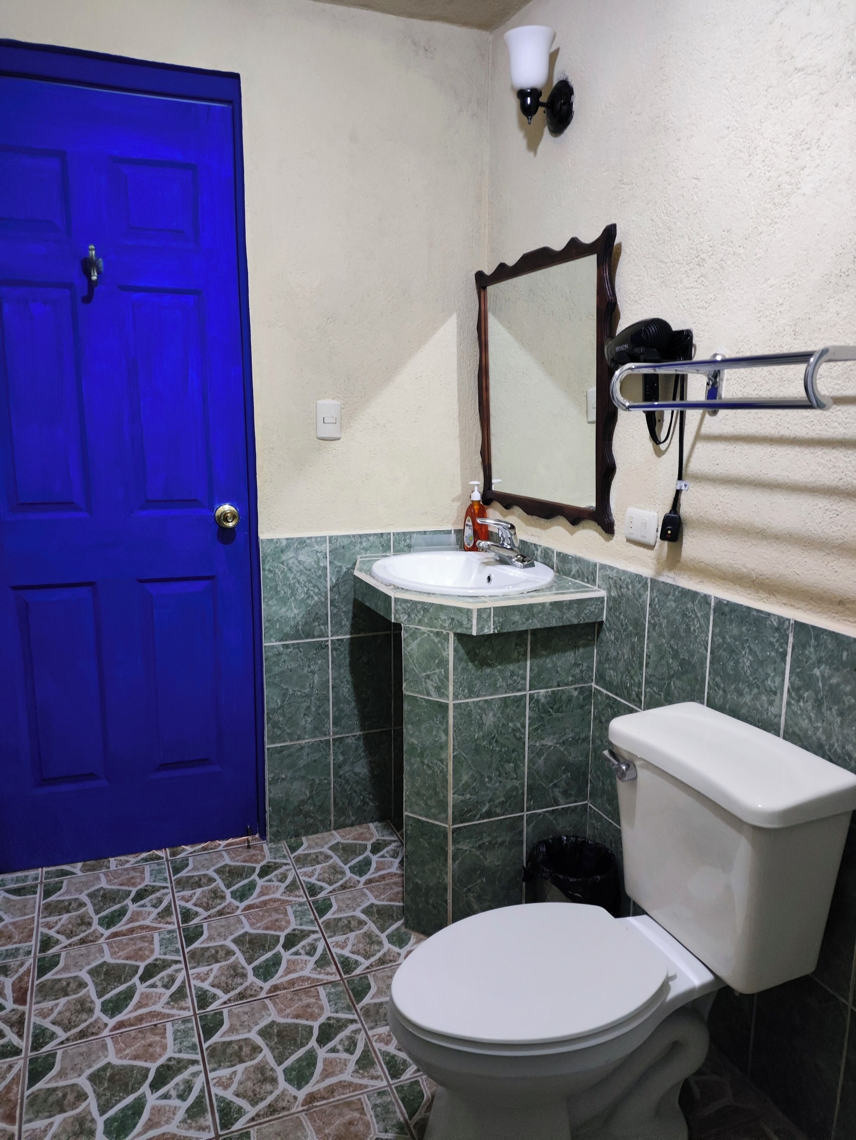 A bathroom with a blue door, a sink, a mirror, a towel rack, and a toilet.