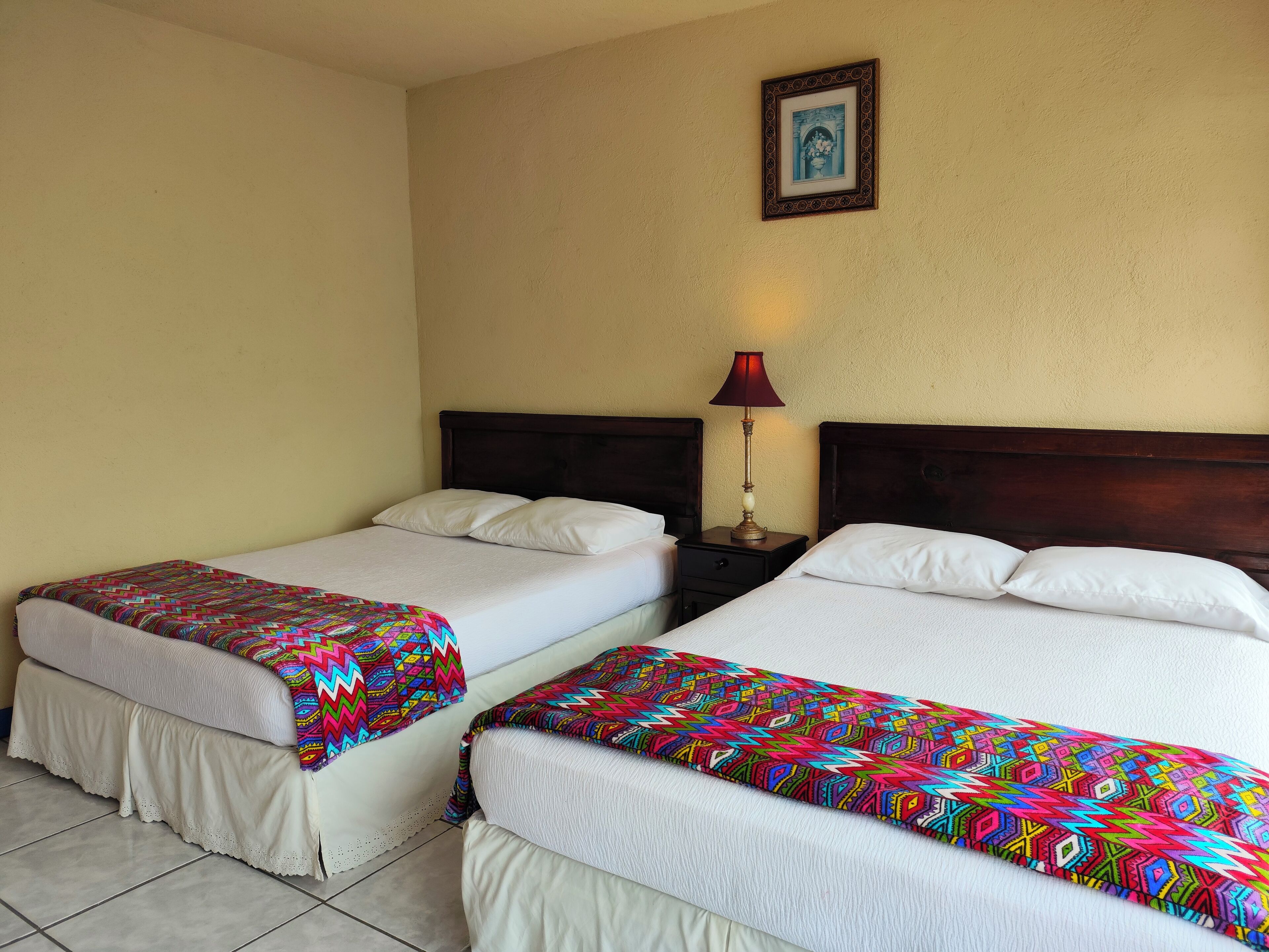 Una habitación de hotel con dos camas, una mesita de noche con lámpara y un cuadro enmarcado en la pared.