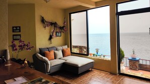 A cozy living room with a sofa, a coffee table, and a view of the sea through large windows. - Hotel La Villa de los Dioses (San Antonio Palopo)