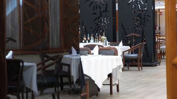 Un restaurante con mesas dispuestas para comer, sillas y una pared decorativa con diseños recortados.