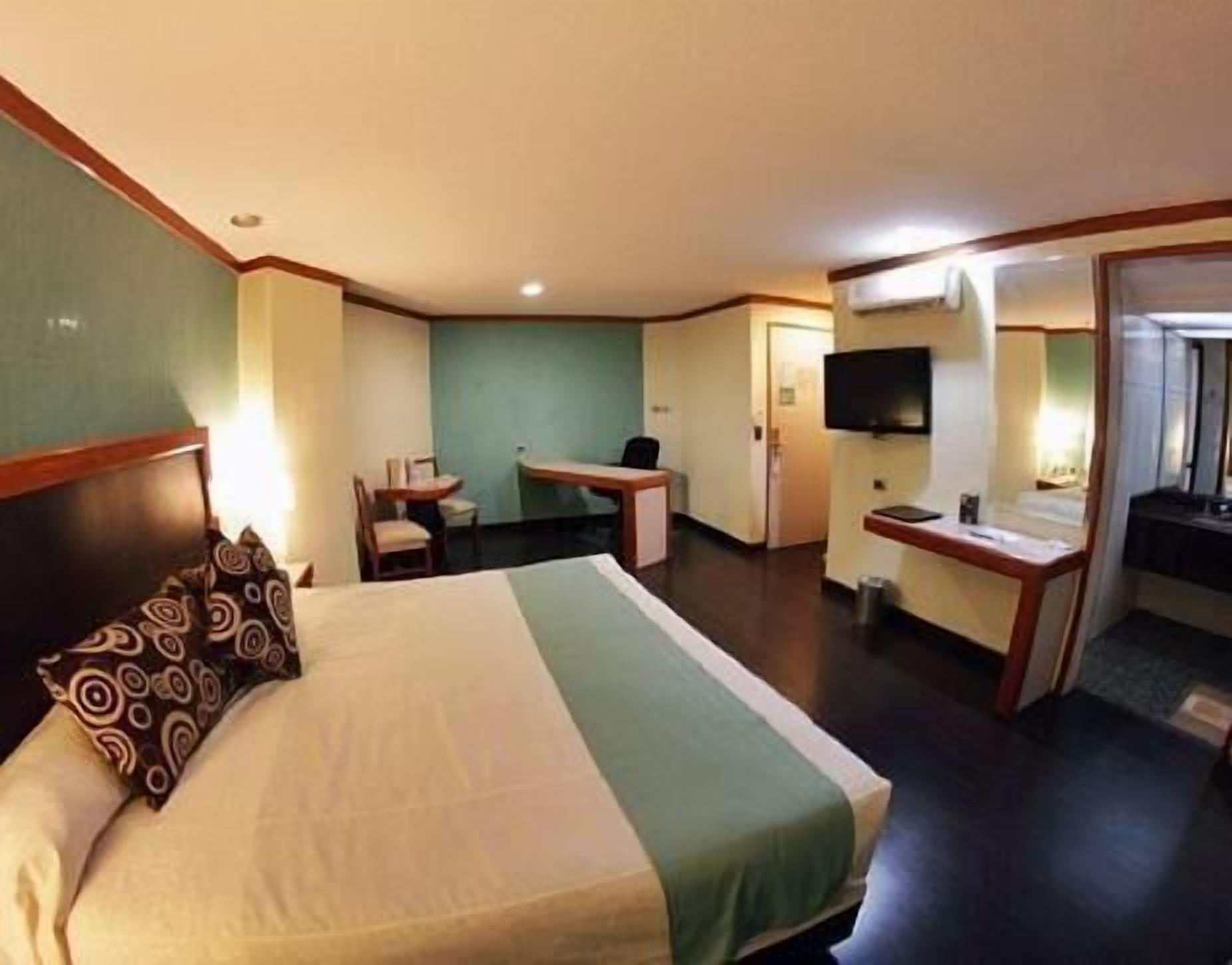 A hotel room with a bed, desk, chair, TV, and a bathroom.