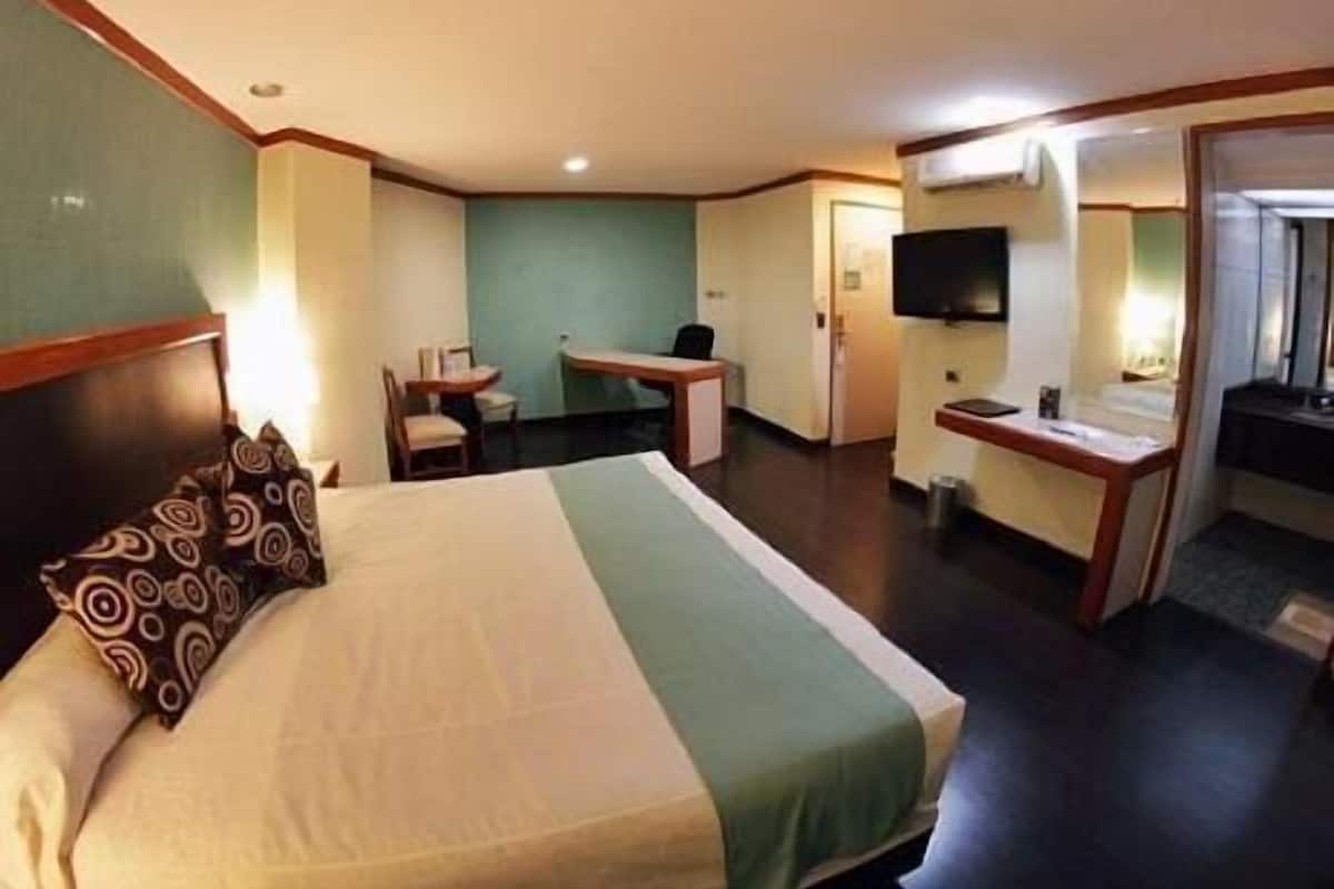 Habitación de hotel con cama, escritorio, silla, televisor y baño.