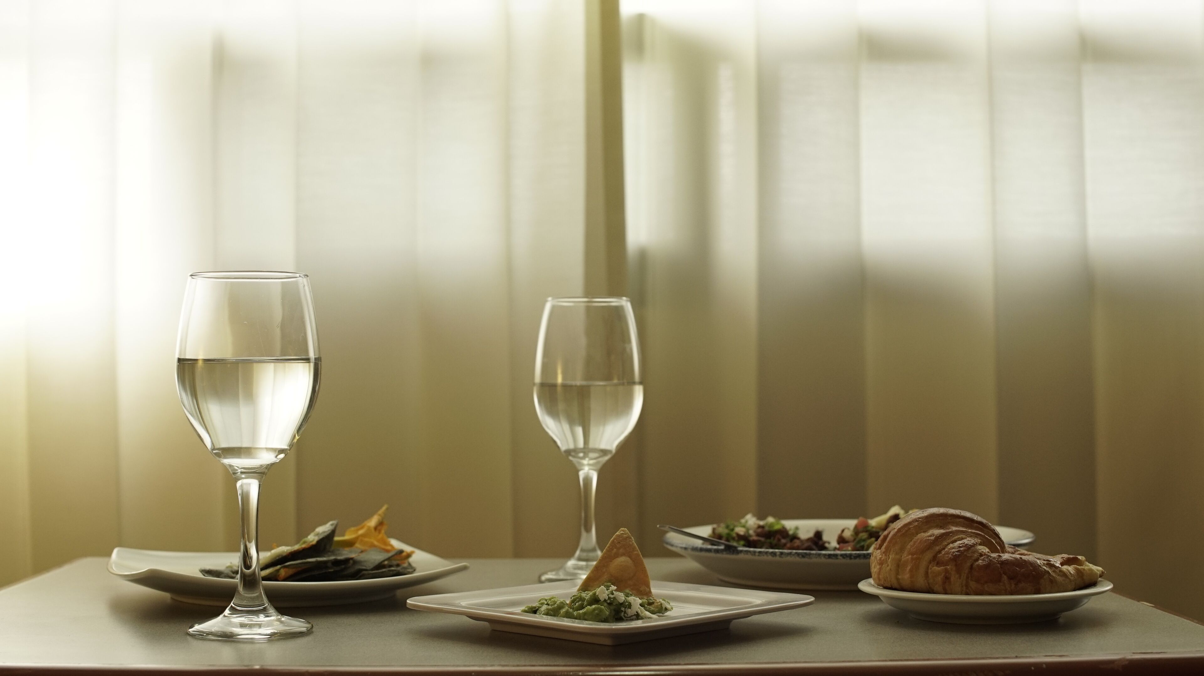 A table with two glasses of water, a plate with a croissant, and a plate with a salad.