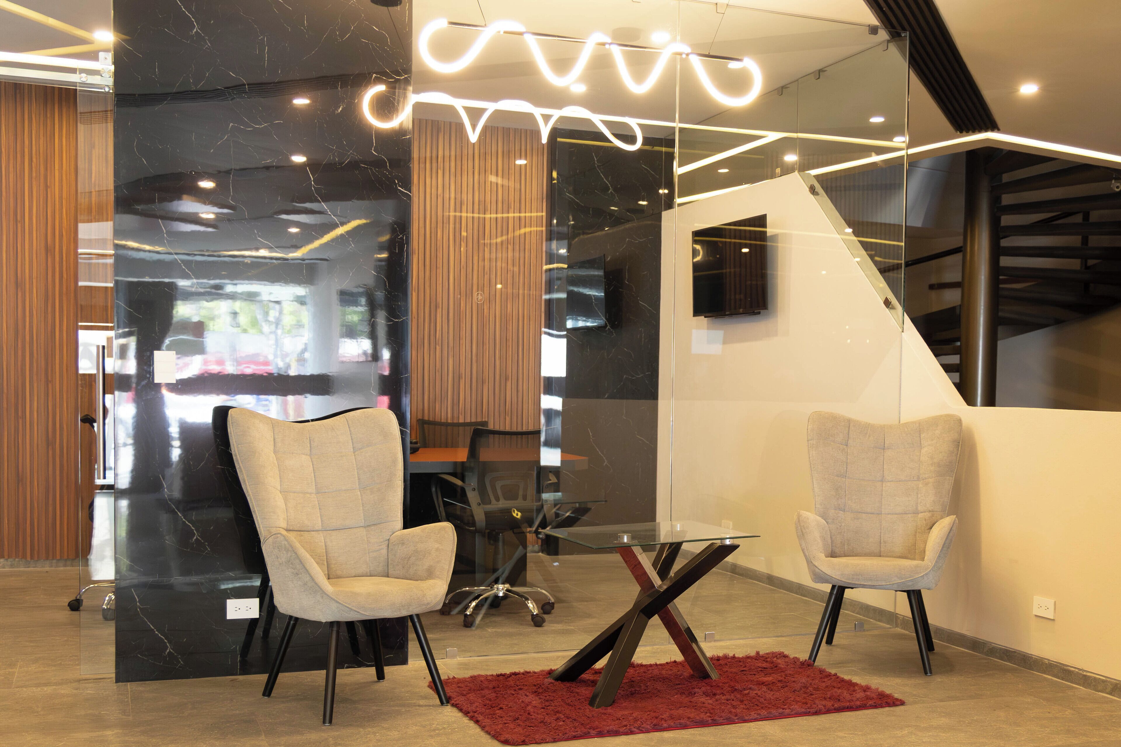 A modern interior with two upholstered chairs, a glass table, and a red rug.
