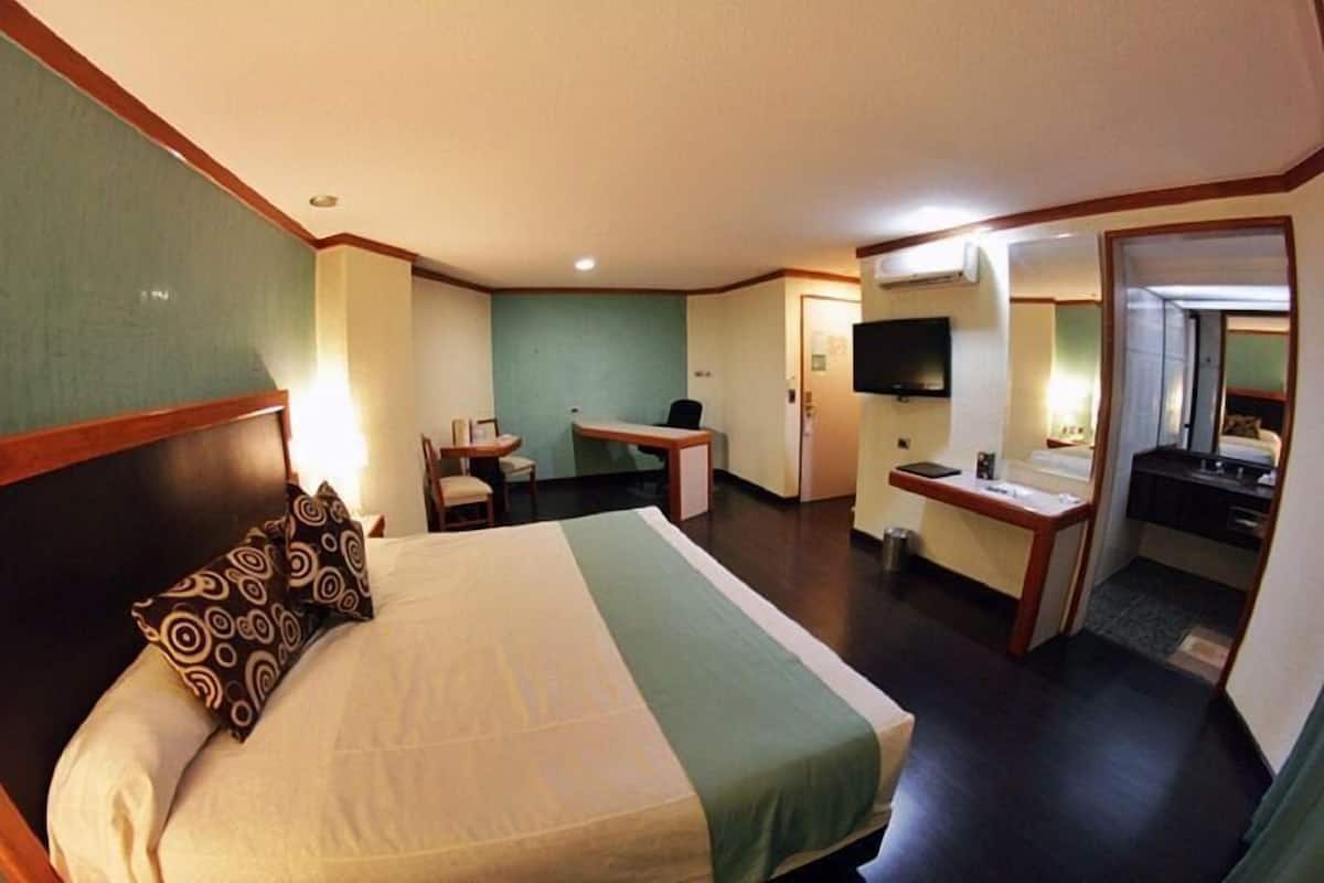 A hotel room with a bed, a desk, a chair, a TV, and a bathroom.
