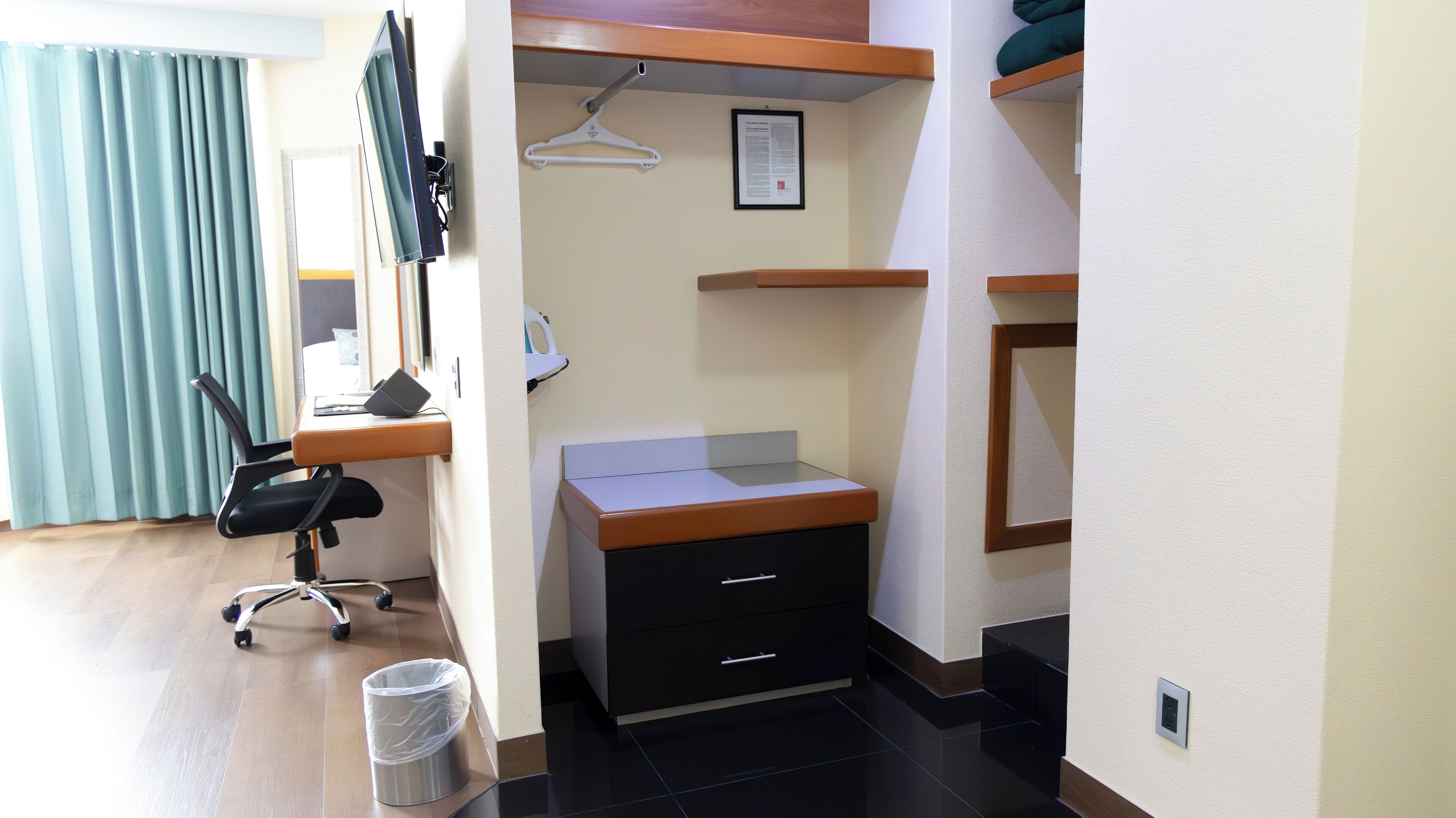 A hotel room with a desk, chair, and a small trash bin.