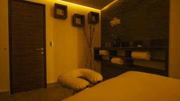 A hotel room with a wooden door, a white pillow, a wall-mounted shelf with towels, and a vase with flowers.