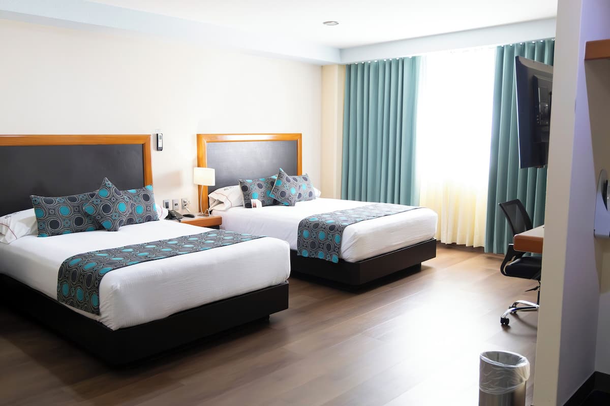 A hotel room with two beds, a desk, a chair, and a TV.