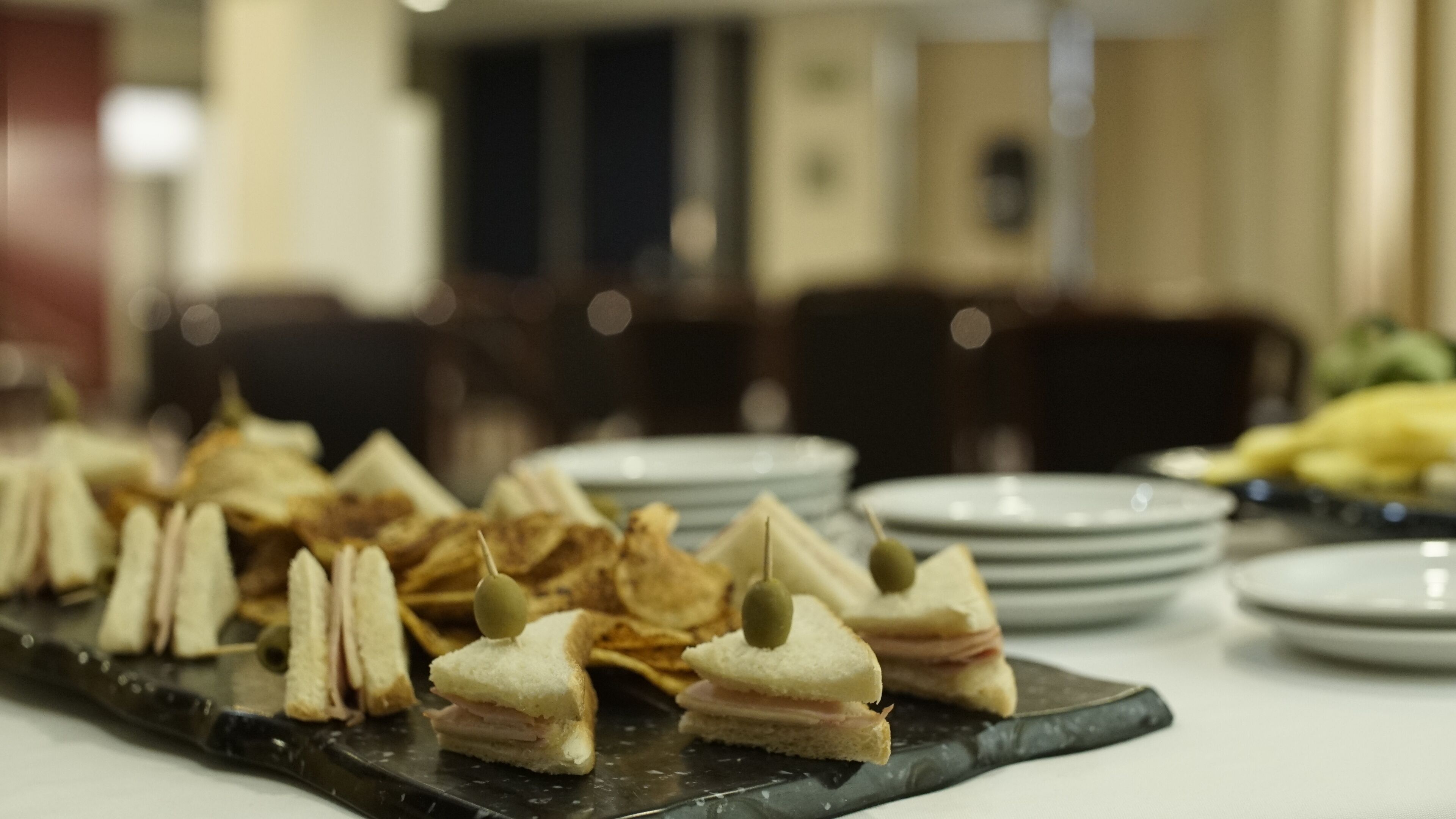 A buffet table with sandwiches, chips, and plates.