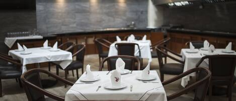 A restaurant with tables set for dining, chairs, and a dark tiled backsplash.