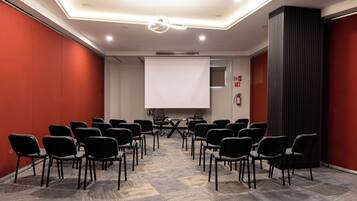 A conference room with rows of chairs facing a projection screen, a whiteboard, and a fire extinguisher on the wall.