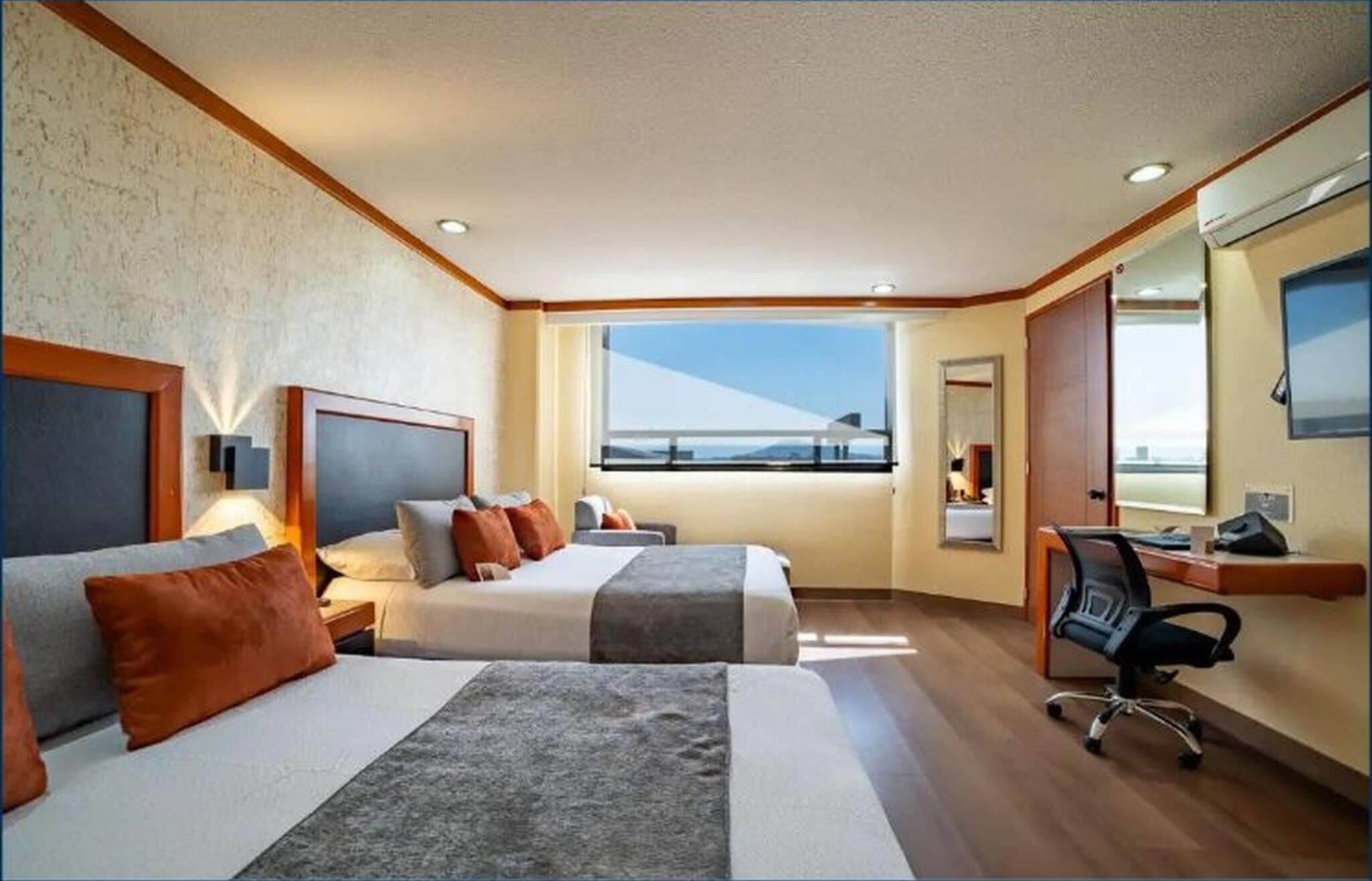 Habitación de hotel con dos camas, un escritorio, una silla, un ventanal con vistas y un espejo.