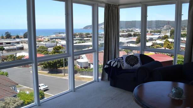 A room with large windows offering a view of a coastal town and the sea. - The Menai Hotel Motel (South Burnie)