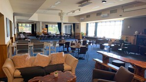 A spacious indoor area with multiple tables and chairs, a large window providing natural light, and a ceiling with recessed lighting and ventilation. - The Menai Hotel Motel (South Burnie)