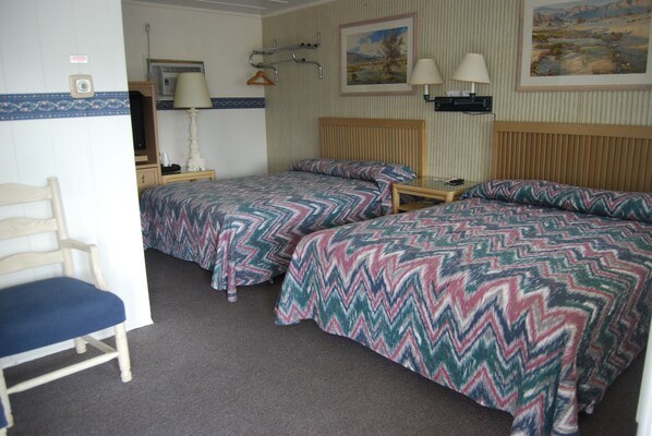 A room with two beds, a chair, a nightstand, a lamp, and a painting on the wall.