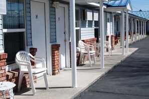 A row of motel rooms with white walls, brick accents, and white plastic chairs. - Redwood Motel (Bridgeport)