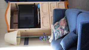 A room with a wooden cabinet containing a flat-screen TV, a blue sofa with patterned cushions, and a small plant. - Redwood Motel (Bridgeport)