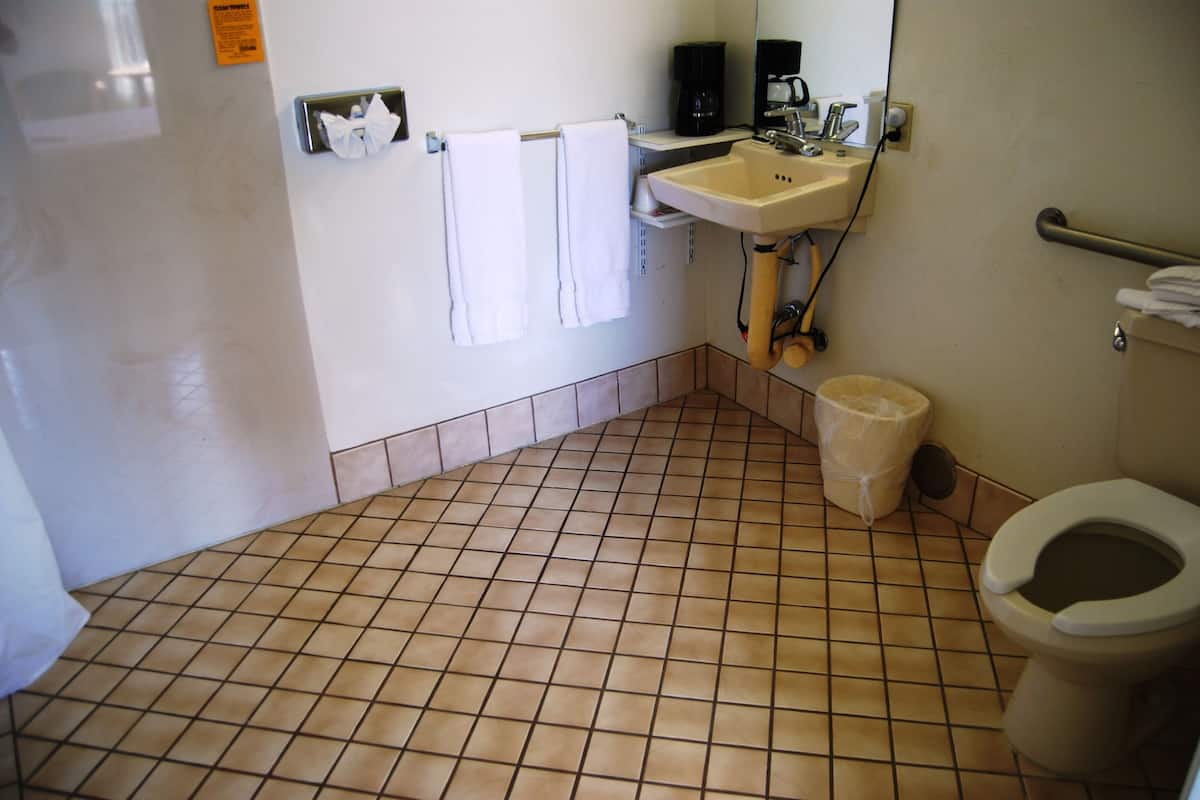 A bathroom with a tiled floor, a sink, a toilet, and a trash can.