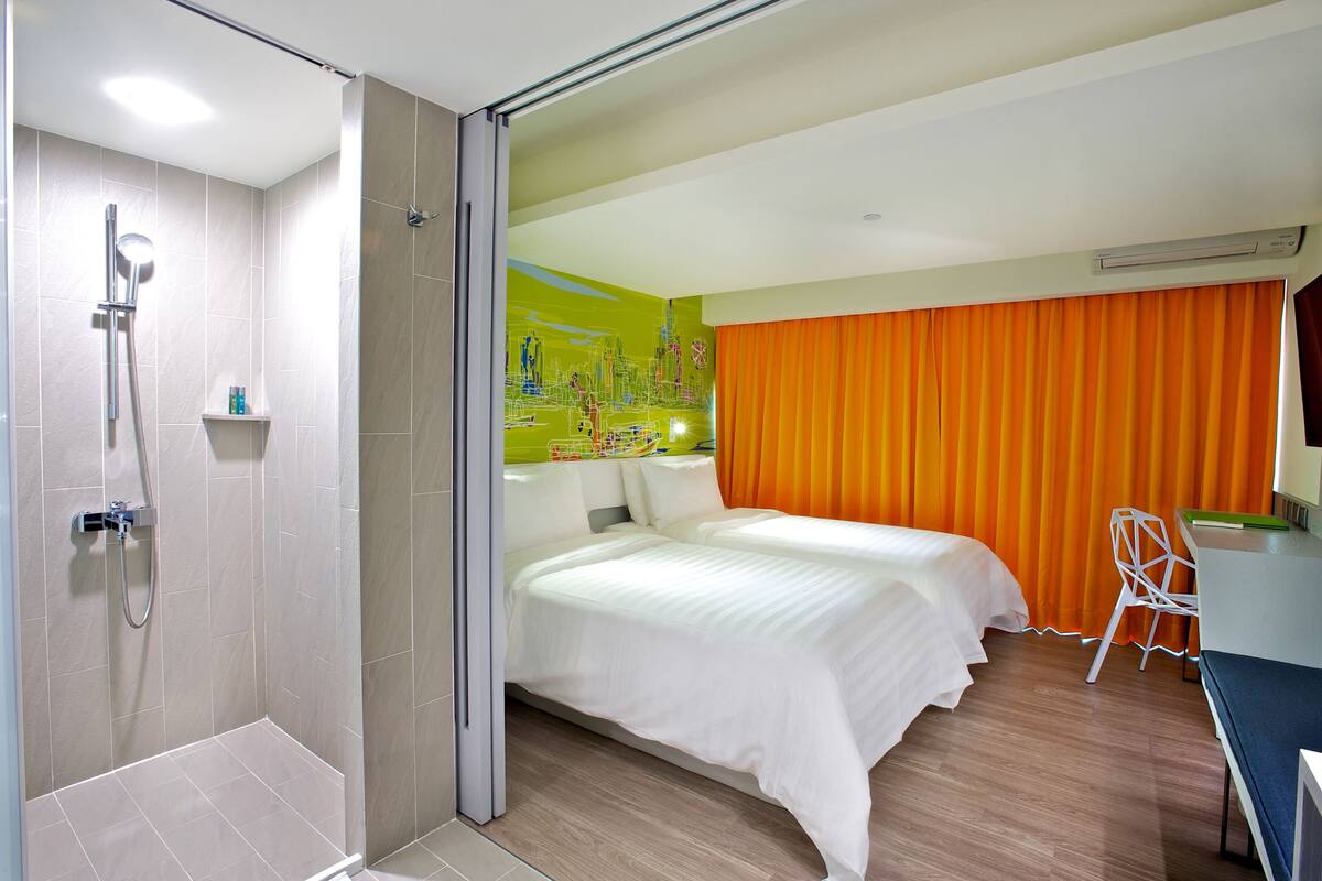 Ein Hotelzimmer mit Dusche, einem Bett, einem Schreibtisch und einem orangefarbenen Vorhang.