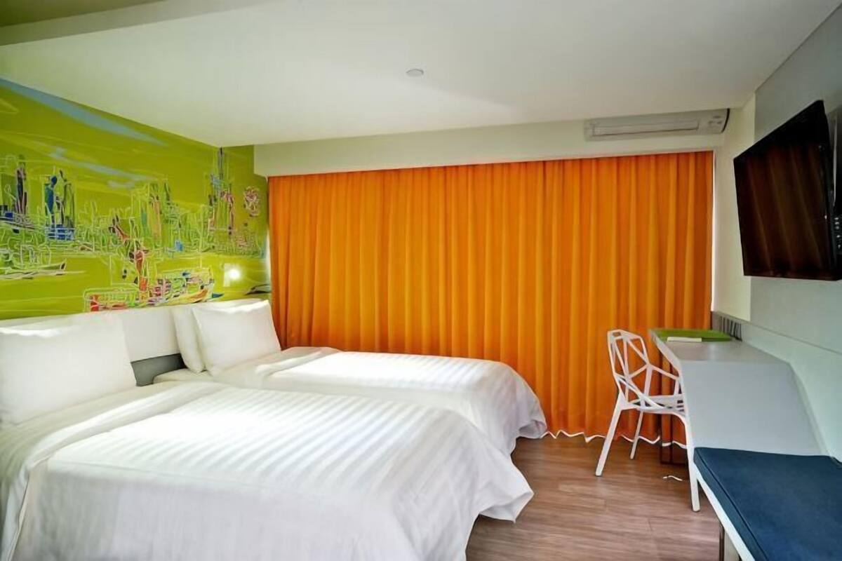 Ein Hotelzimmer mit zwei Betten, einem Schreibtisch, einem Stuhl, einem Fernseher und einem Wandgemälde.