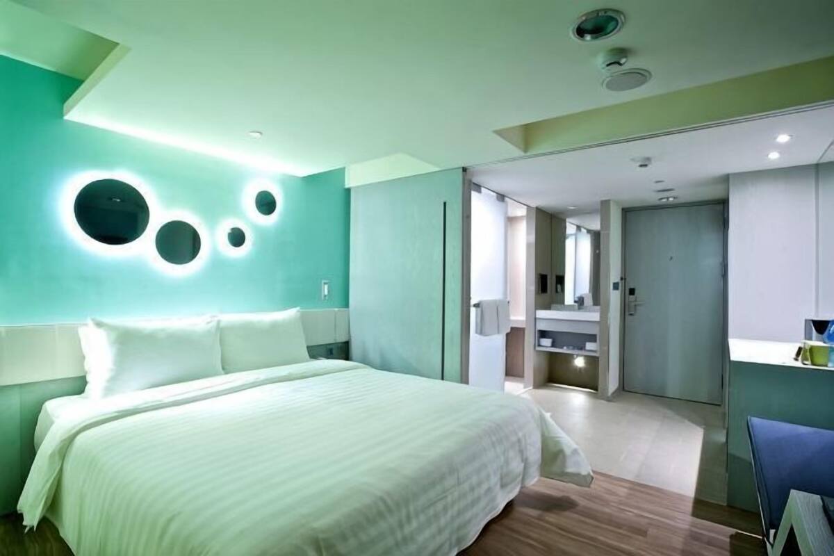 Ein modernes Hotelzimmer mit einem großen Bett, einem Schreibtisch und einem durchgegangenen Tür sichtbaren Badezimmer.