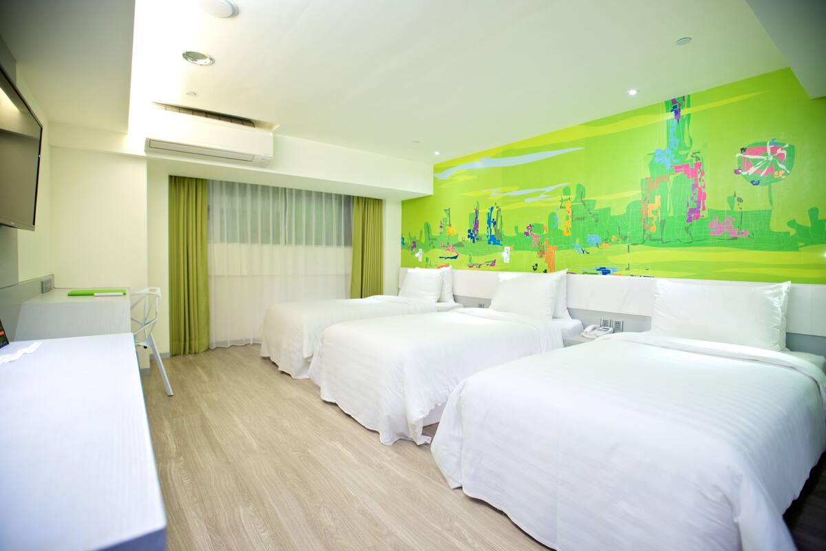 Ein Hotelzimmer mit zwei Betten, einem Schreibtisch und einem großen Fenster mit Vorhängen.