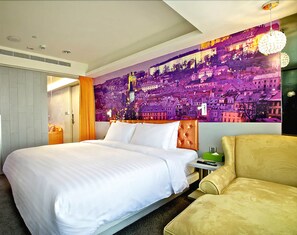 Ein Hotelzimmer mit einem großen Bett, einer Couch, einem Stadtbild-Wandgemälde und einer Tür zu einem weiteren Raum.