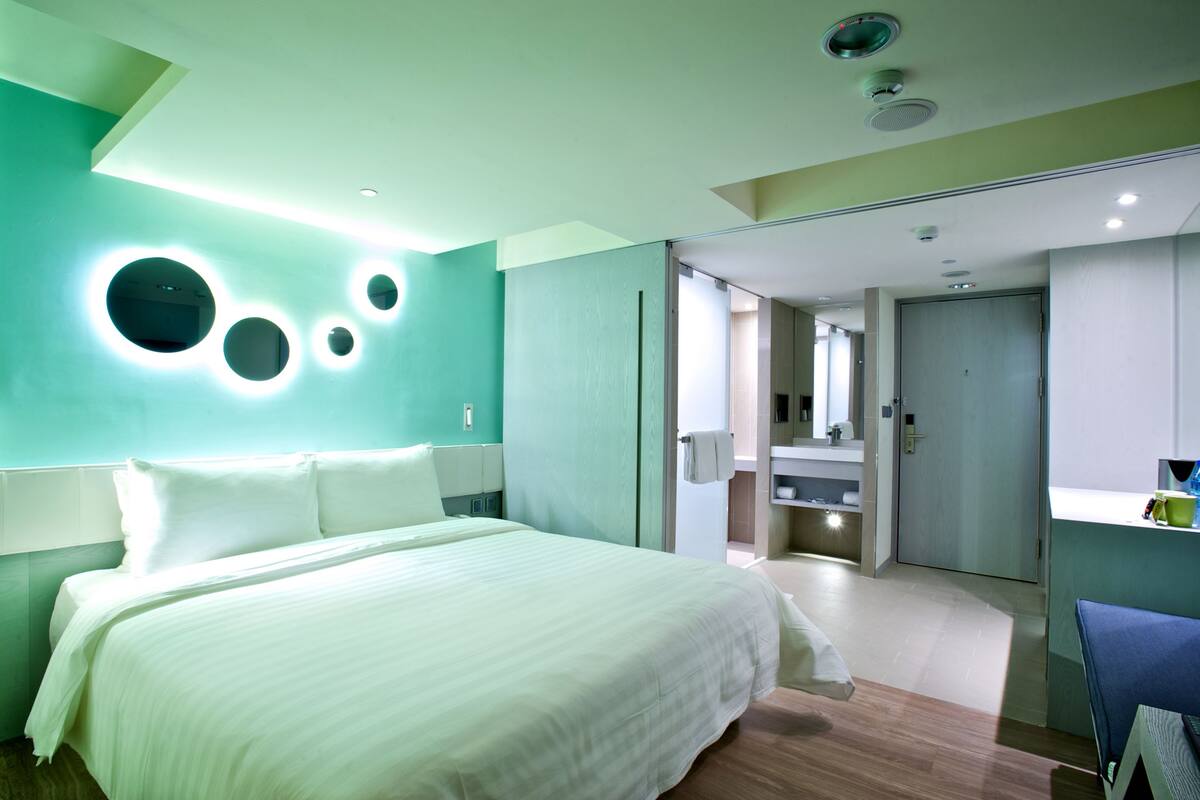 Ein modernes Hotelzimmer mit einem großen Bett, einem Badezimmer mit Spiegel und einem Schreibtisch mit Stuhl.
