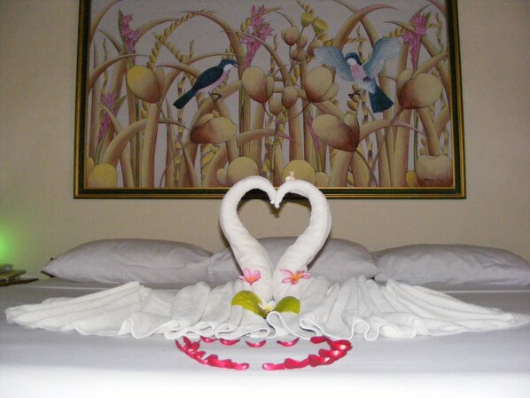 A bed with a heart-shaped towel arrangement and a painting of birds and flowers in the background.