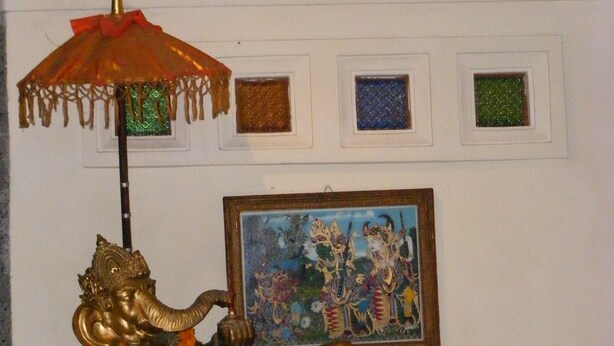 A statue of a reclining deity with an umbrella, a framed painting, and a Buddha figure above. - Jalan Jalan Villas & Spa (Ubud)