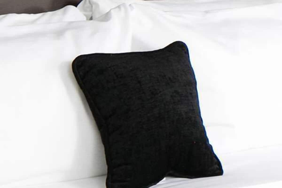 A bed with white bedding and a single black pillow.