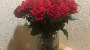 A clear glass vase with a floral arrangement of red roses on a wooden table against a textured wall.