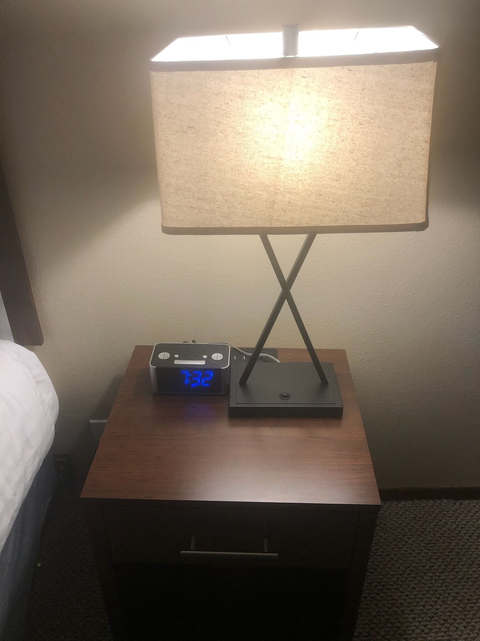 A bedside table with a lamp, a digital clock, and a power strip.