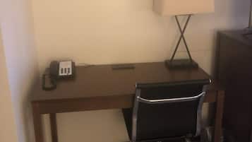 Quarto de hotel com escrivaninha de madeira, cadeira de escritório preta, luminária de mesa e telefone.