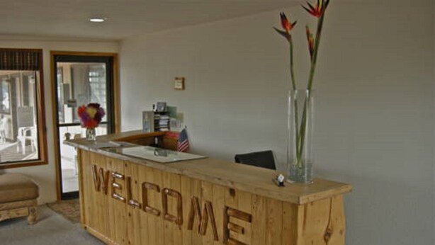 A wooden reception desk with a 'WELCOME' sign, a vase with flowers, and a rug on the floor. - Red Lion Inn & Suites La Pine (La Pine)