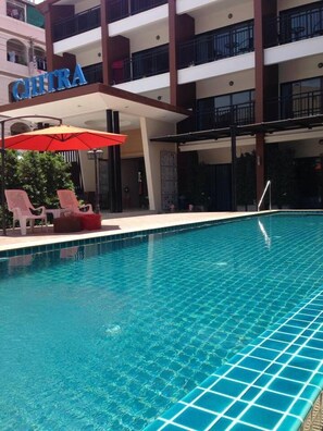 A swimming pool with lounge chairs and an umbrella, surrounded by a building with balconies and the name "CHITRA" visible. - Chitra Suite (Pattaya)