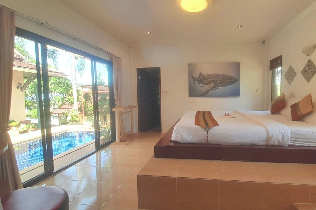 A spacious bedroom with a large bed, a view of a swimming pool, and a wall with a shark painting.