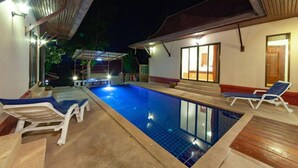 A swimming pool with lounge chairs, a covered area, and a building with a wooden roof and glass doors. - Samui Diving Resort (Koh Samui)